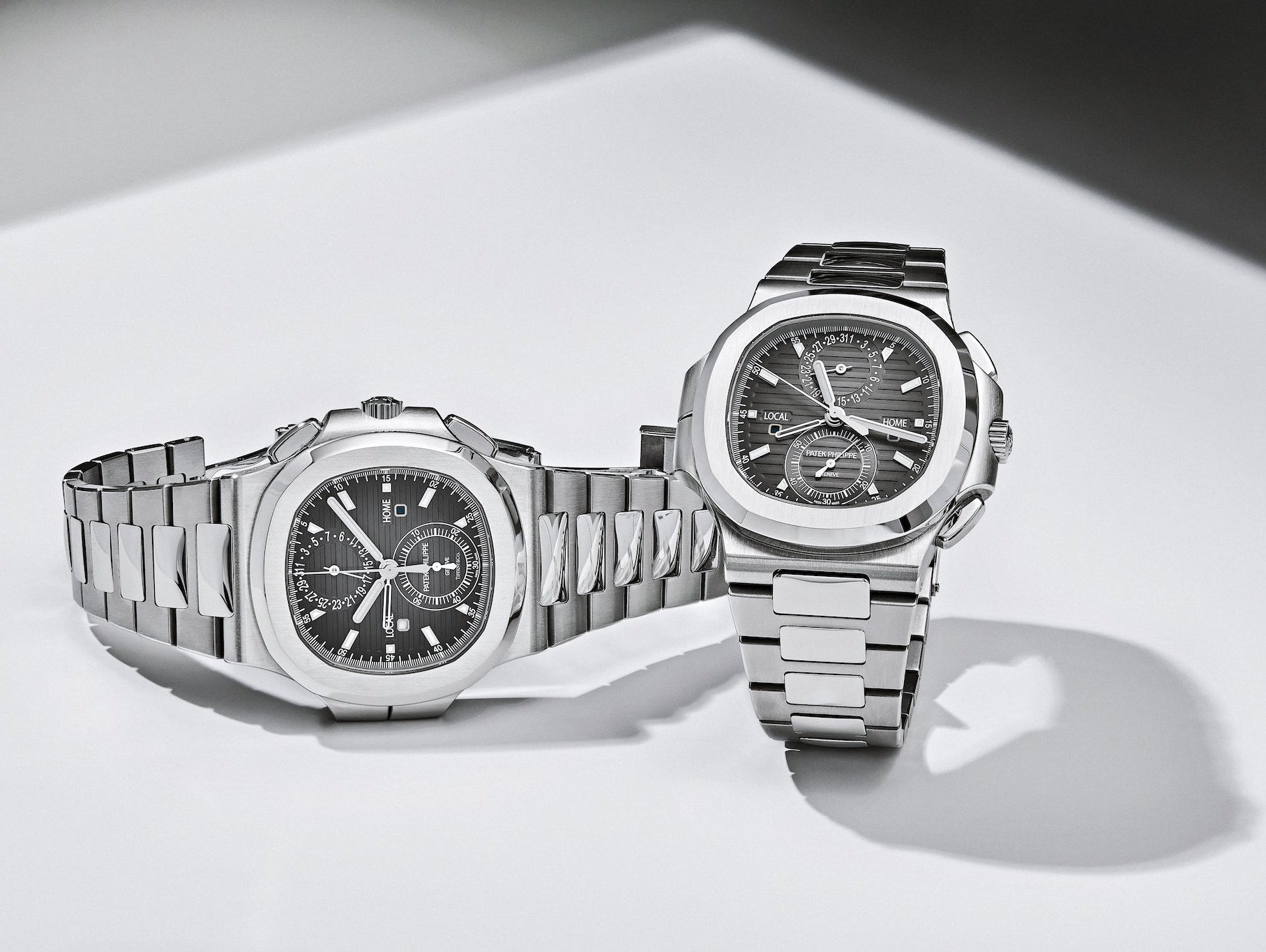 Patek Philippe Nautilus Travel Time 5990 on its side next to a Patek Philippe Nautilus Travel Time 5990 Tiffany & Co. dial standing upright