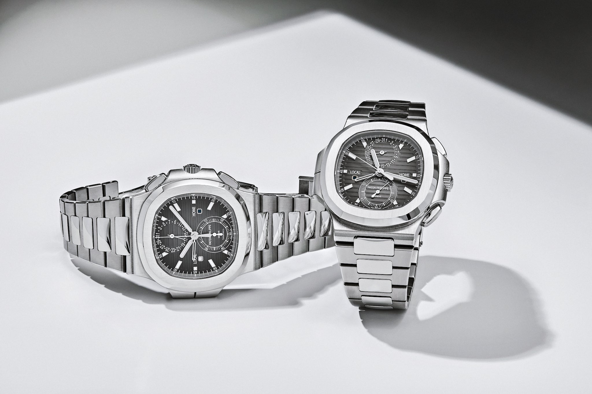 Patek Philippe Nautilus Travel Time 5990 on its side next to a Patek Philippe Nautilus Travel Time 5990 Tiffany & Co. dial standing upright